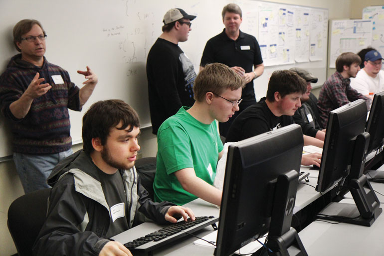 nonpareil CEO Dan Selec, instructor Aaron Winston and College of Engineering professor Gary Spivey look on as students diagnosed with autism create gaming software on the George Fox University campus.