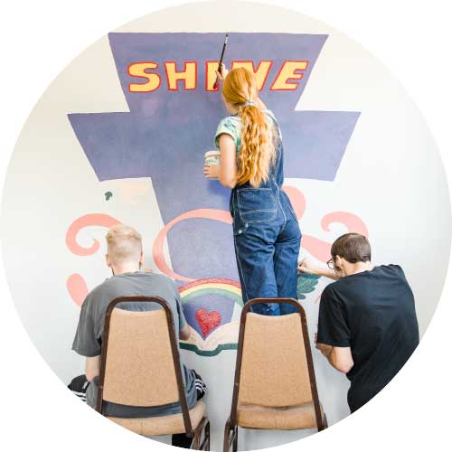 Photo of three art students painting a mural on serve day.