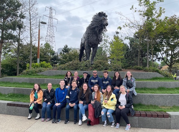 Students sit in front of a metal sculpture of a lion