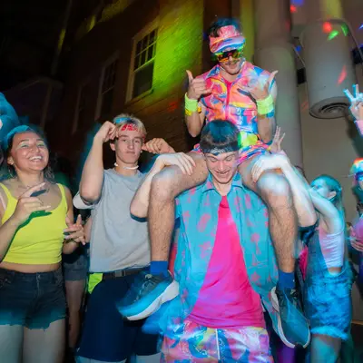 A student sits on his friend's shoulders and poses at the 80's dance