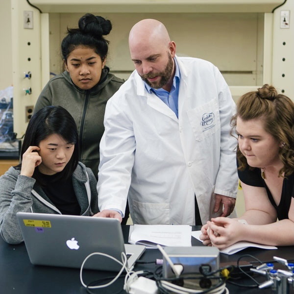 Professor works 3 students on a computer