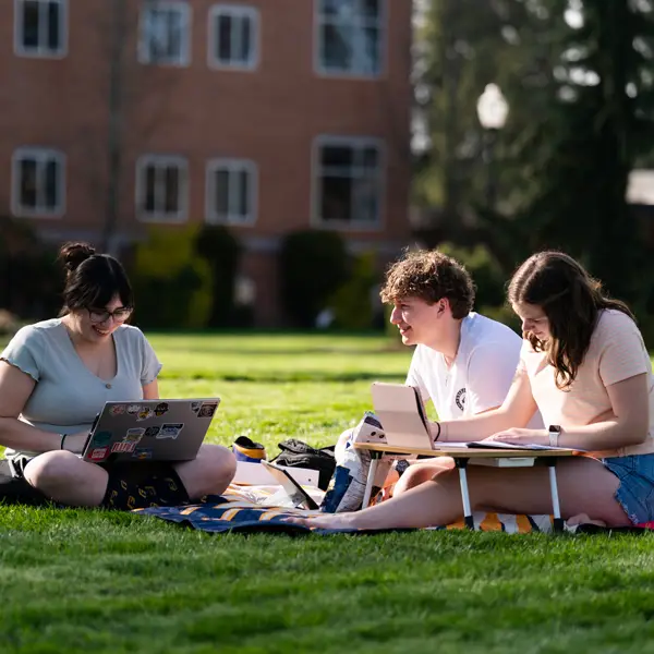 Three students sitting on a blanket in the quad working and conversing