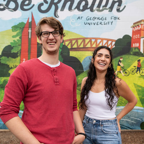 students laugh in front of a mural