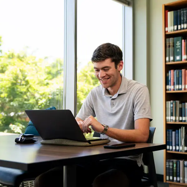 Online student works in a library on his laptop