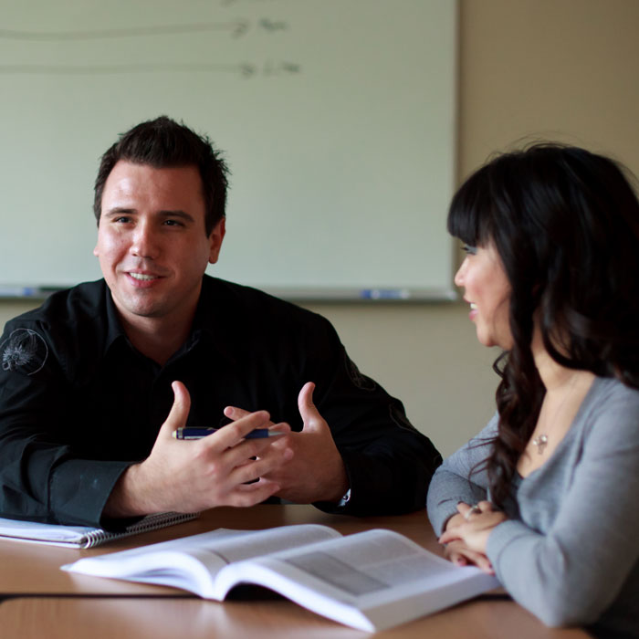 An adult student sits at a desk with a peer while they work on an assignment