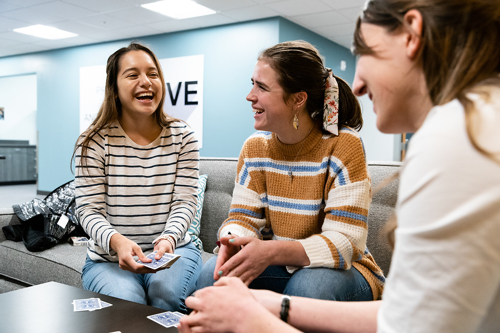 Three girls laugh while playing a card game