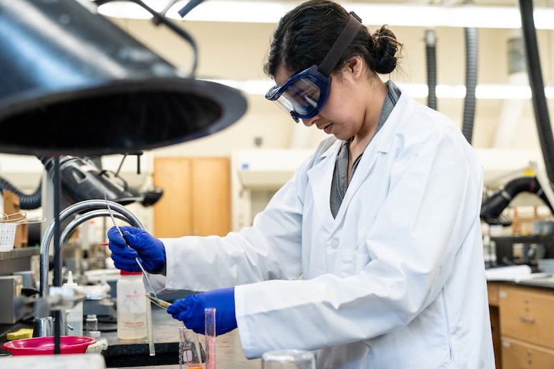 A student in a lab coat and goggles studies materials