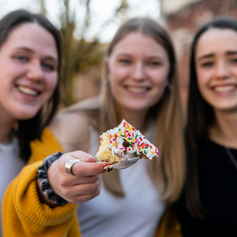 Three girls eat a piece of cake with sprinkles