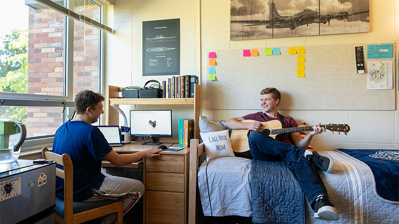 Two students have a conversation in a dorm room