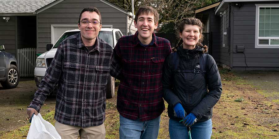 three students smiling with trash in hand