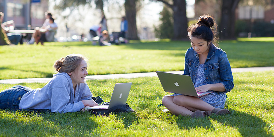 two students on computers outside