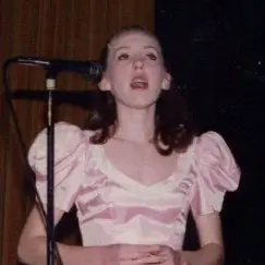 Hayley Cummings as a child singing into a mic wearing a pink frilly dress