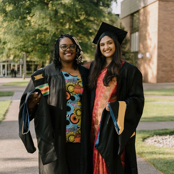 Rachel smiling next to a friend in their caps and gowns