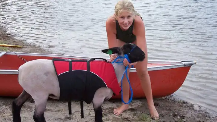 Allison standing at the edge of some water smiling with a sheep