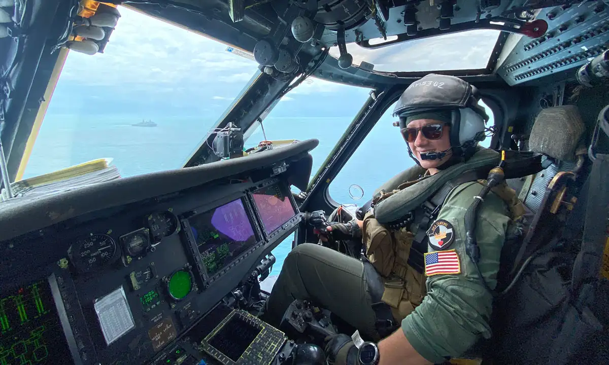 Allison Moss sitting in the cockpit of her helicopter, in the air, smiling at the camera