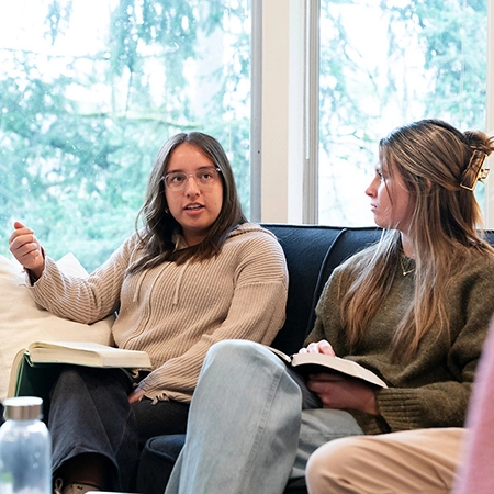 Two students on the couch, talking while holding open their Bible