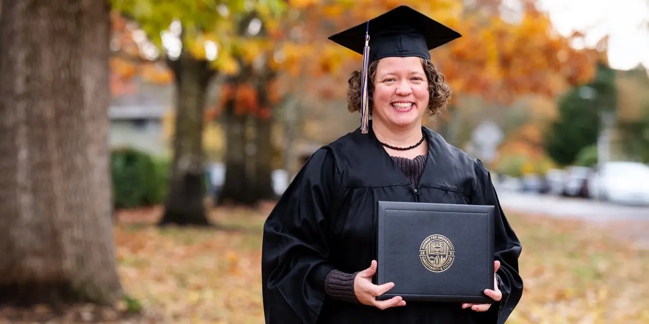Lisa Jones smiles in cap and gown and holds her graduate degree