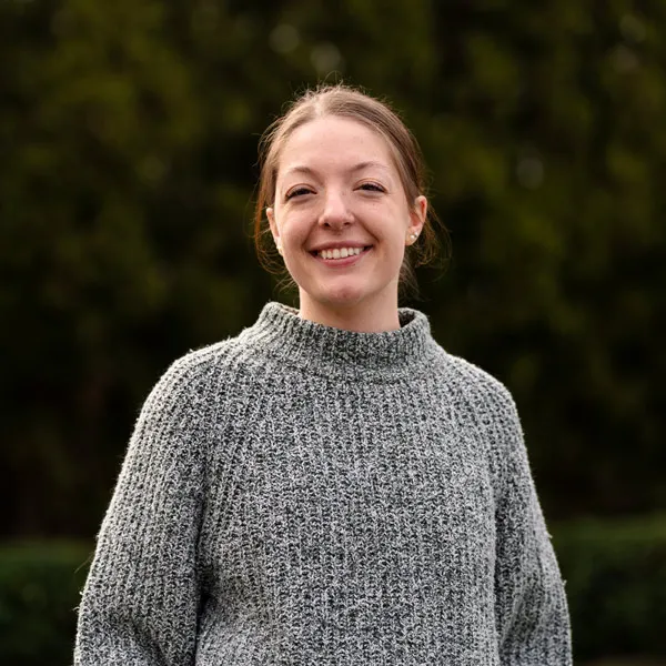 Clark smiles for a photo outside, wearing a grey knit sweater