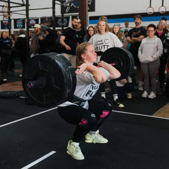 Adri Salazar performs a front bar squat in a gym while a crowd looks on