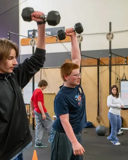Two young boys lift barbells in a group fitness class