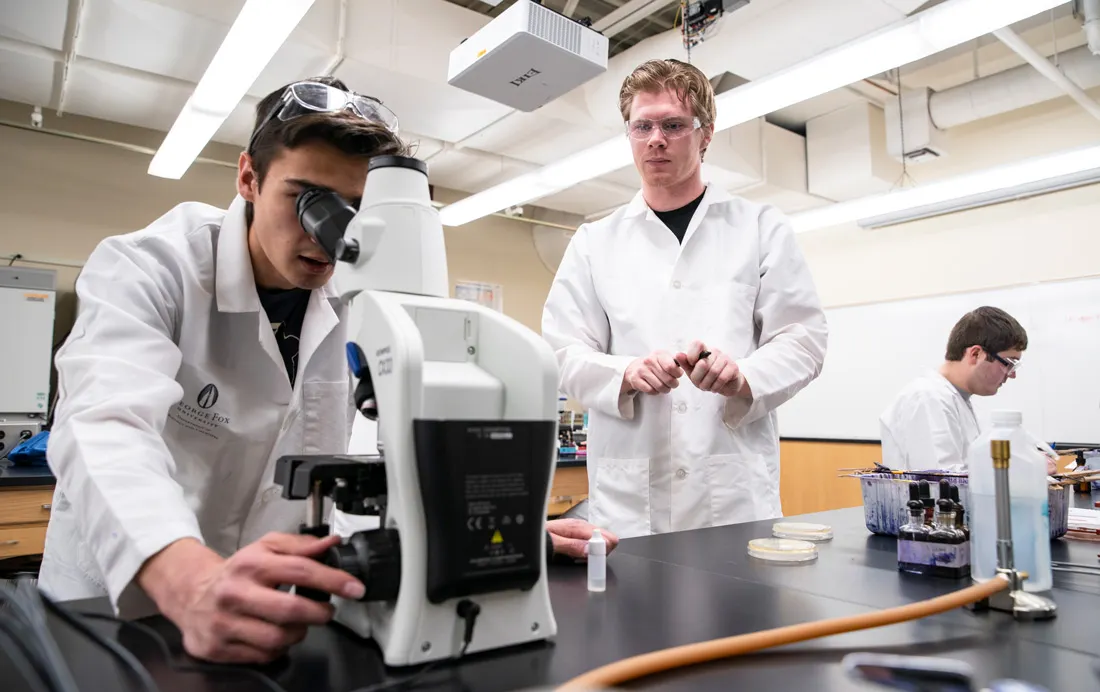One student looks through a microscope while his partner looks on 