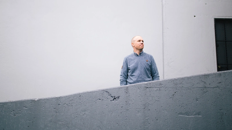 Ben standing by a concrete building, while looking to the right