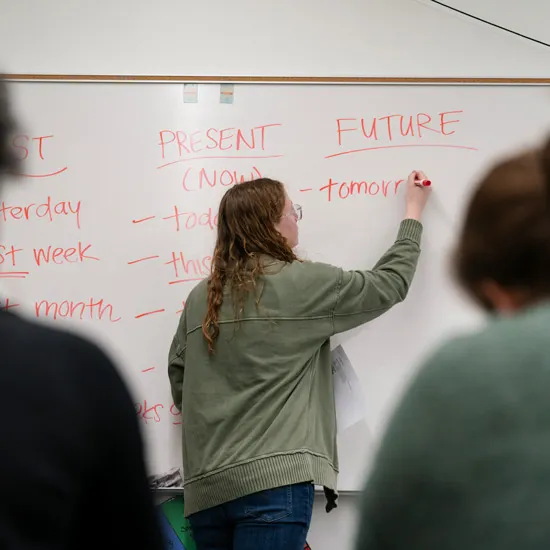 Emmy King writes on a whiteboard in front of class