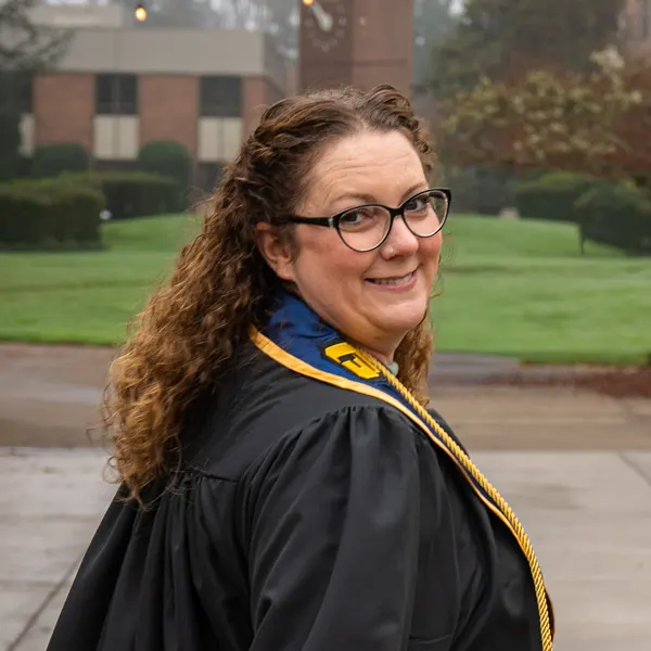 Emilia Reynolds in a cap and gown looks over her shoulder and smiles at the camera