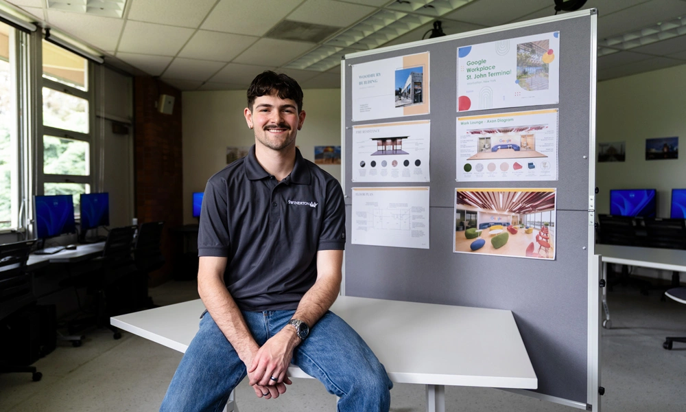 Caleb smiling and sitting in front of a board of his interior design work