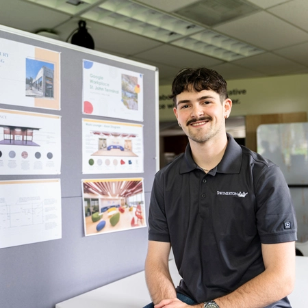 Caleb Parker smiling while sitting in front of his design work