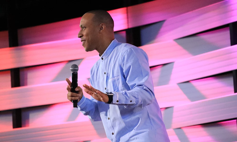 Mario delivering a sermon on stage with a microphone in hand