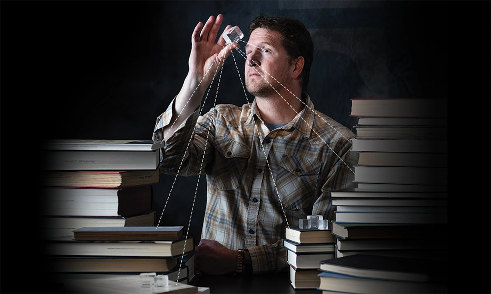 man looking into a clear cube with dotted lines coming from the cube, pointing to nearby books