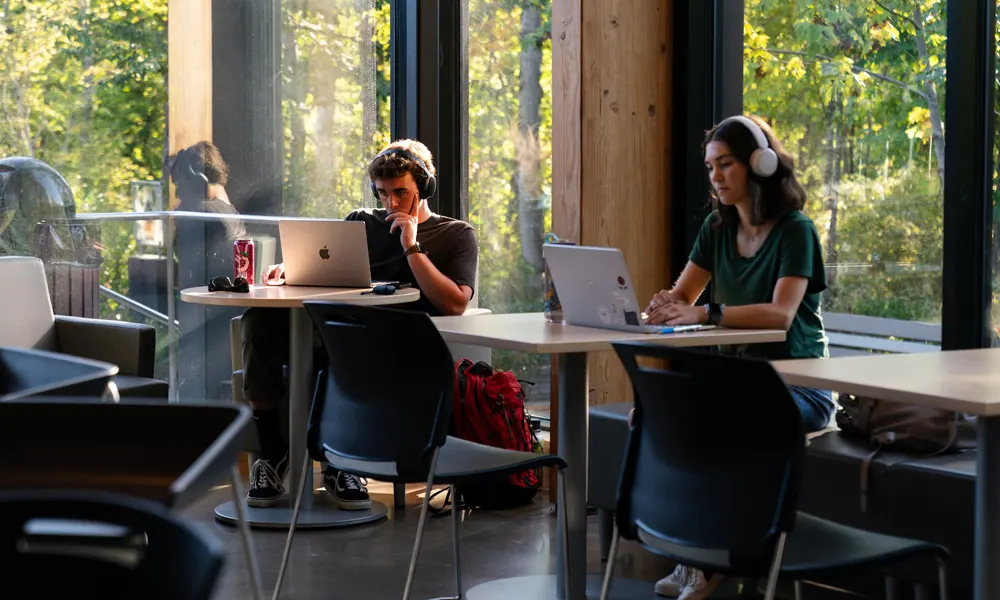 Two students study in the Bridge Cafe in front of the windows