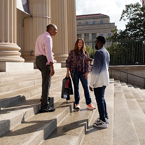 3 people standing on stairs in front of a building having a discussion