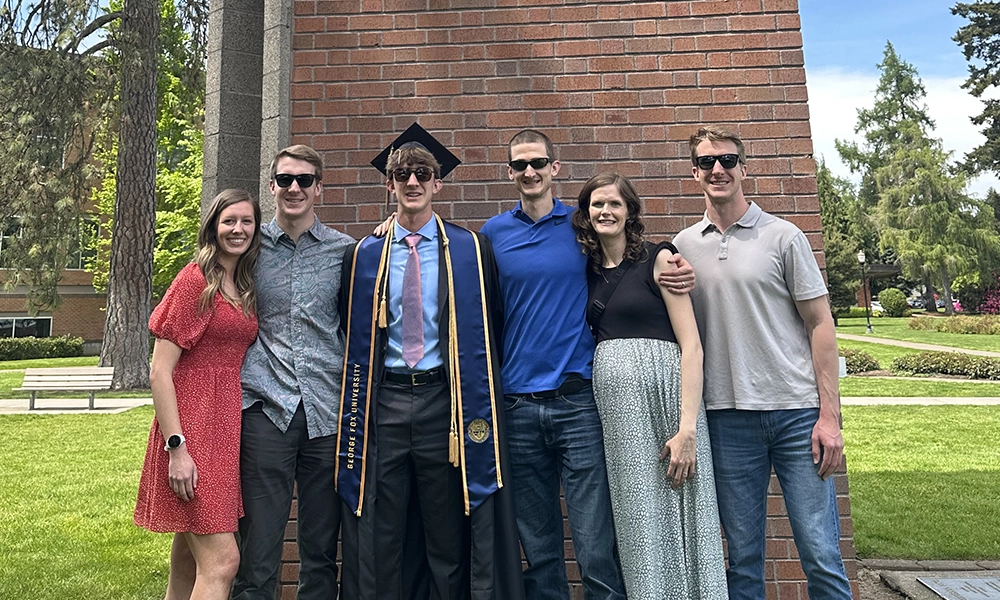 The four brothers and their wives standing in front of the clock tower with sunglasses in Gus's graduation