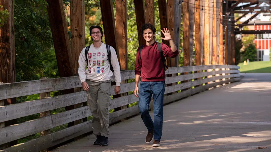Two George Fox students wave while walking on the bridge