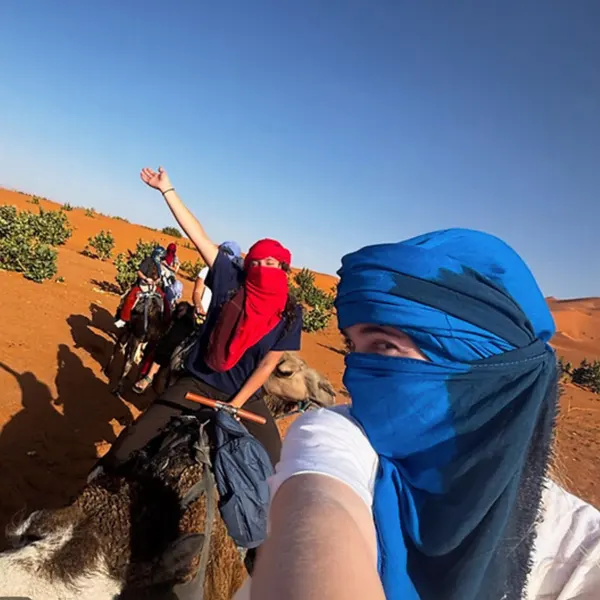 Two excited students with headscarves ride on camels in the desert 