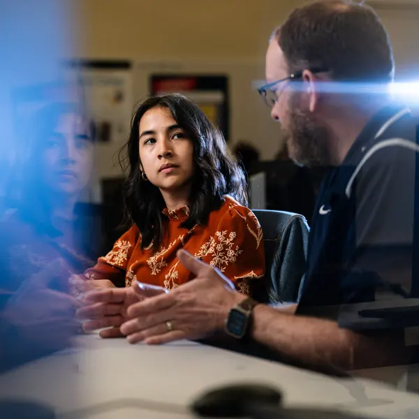 A student works with a professor in a computer lab