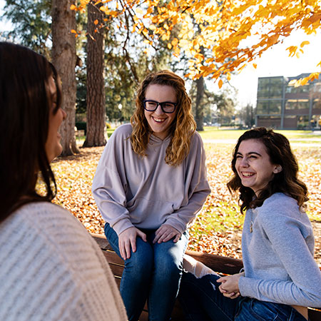 Three friends talking and smiling on campus quad