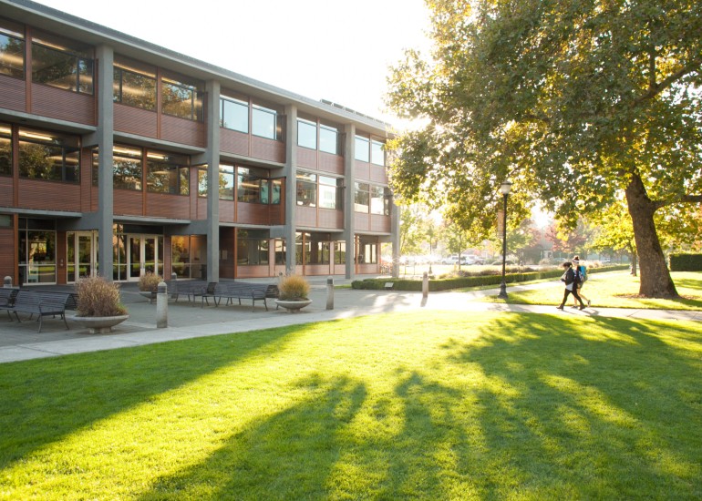 Two students walking across a campus quad with the setting sun behind them