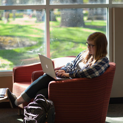 Student sitting on a chair typing on her computer in the library