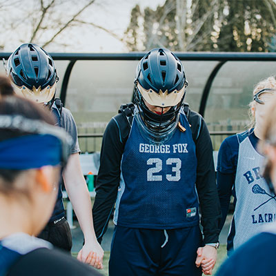 Lacrosse athletes holding hands and praying as a team