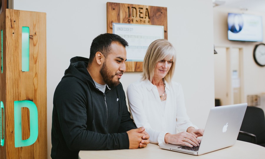 Student and employee standing at a table together looking at a laptop