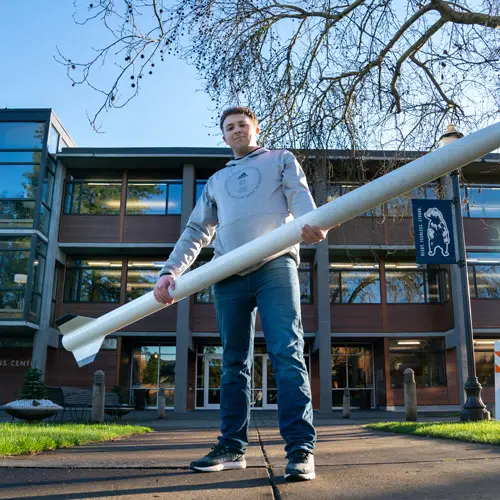 Student Tyler holds a massive rocket on campus