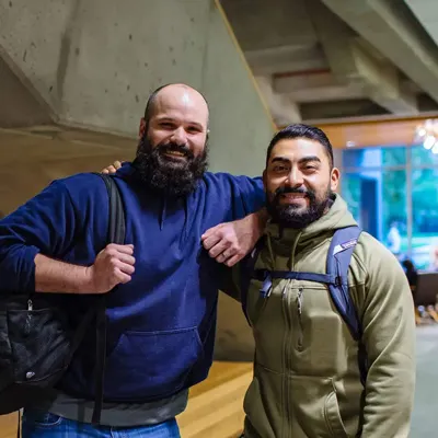 Two veteran students smile with one arm around each other.