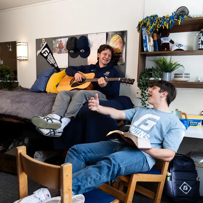 Two male roommates laugh together in their dorm room