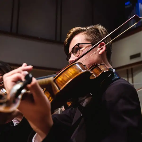 Toma en primer plano de una estudiante tocando el violín durante un concierto