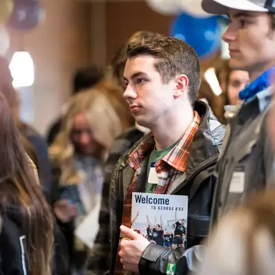 Ethan holding a welcome packet at Bruin Preview standing amongst students and balloons