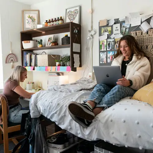 Students in their dorm room interacting, working, and smiling