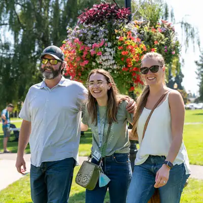 Student smiling and walking through campus with her parents on either side